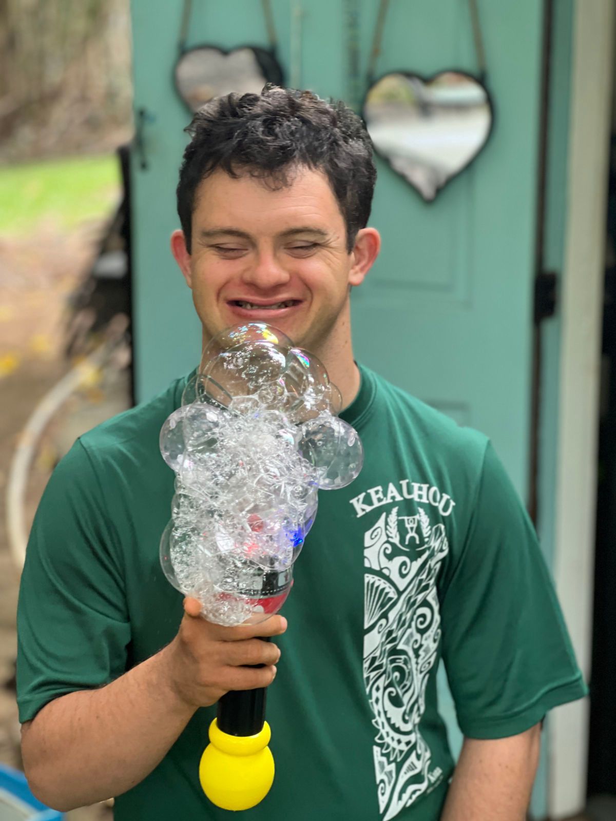 A young man in a green shirt is blowing soap bubbles.