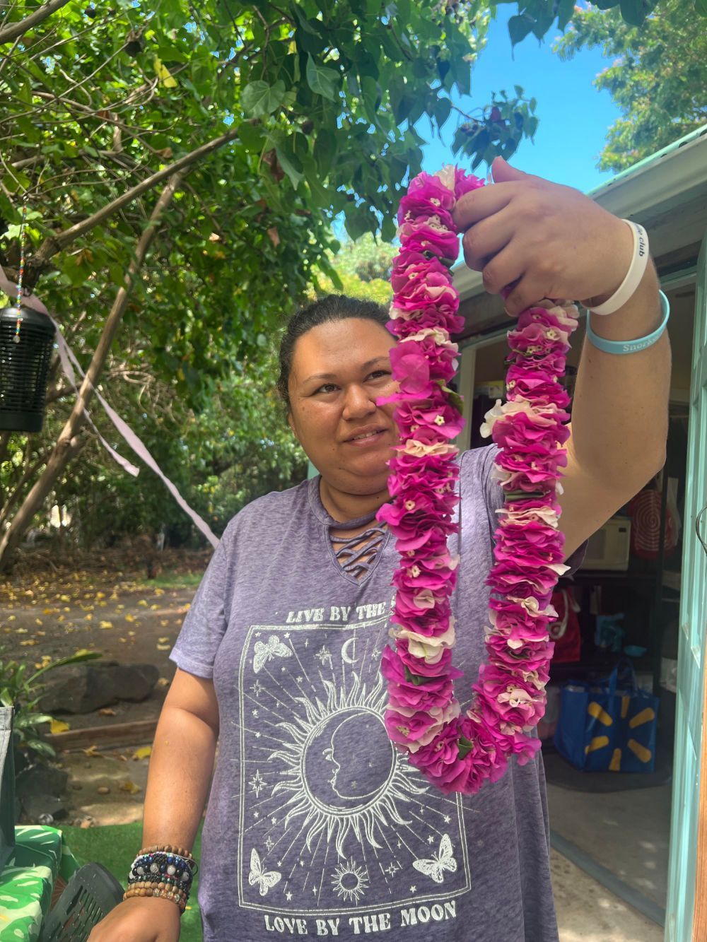 A woman is holding a pink lei in her hands.