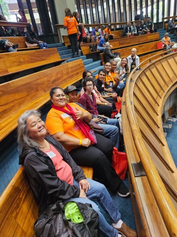 A group of people are sitting on wooden benches in an auditorium.