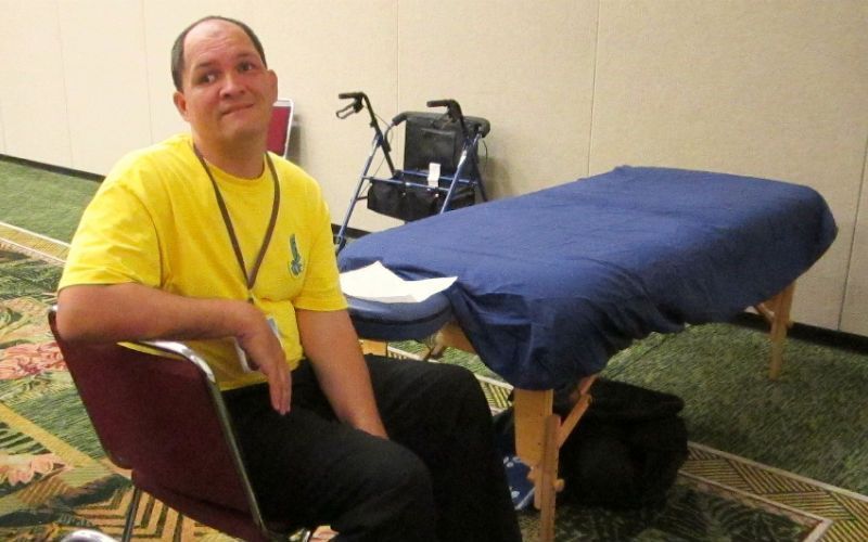 A man in a yellow shirt is sitting in front of a massage table