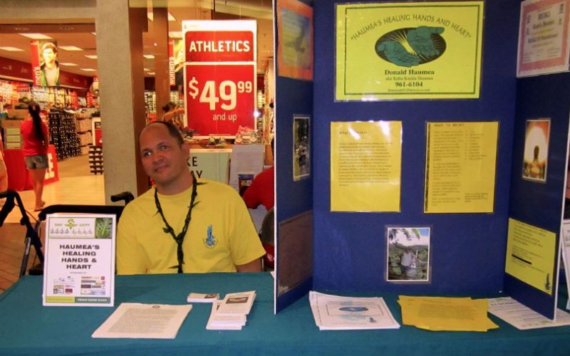 A man sits at a table in front of a sign that says athletics