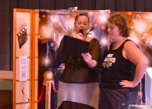 Two women are standing next to each other in front of a movie clapper board.
