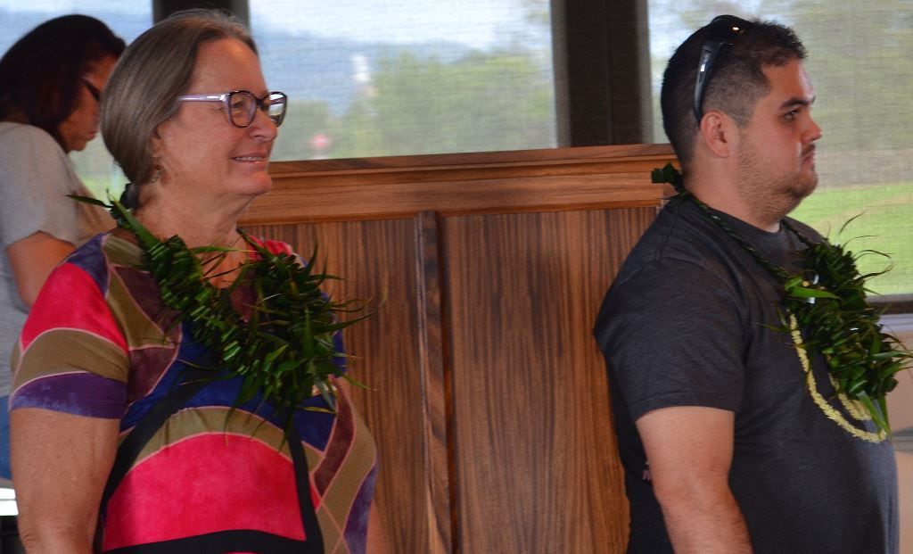 A man and a woman are standing next to each other wearing lei.