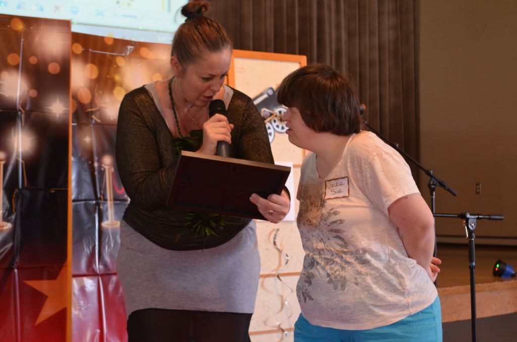A woman is holding a clipboard and speaking into a microphone while another woman looks on.