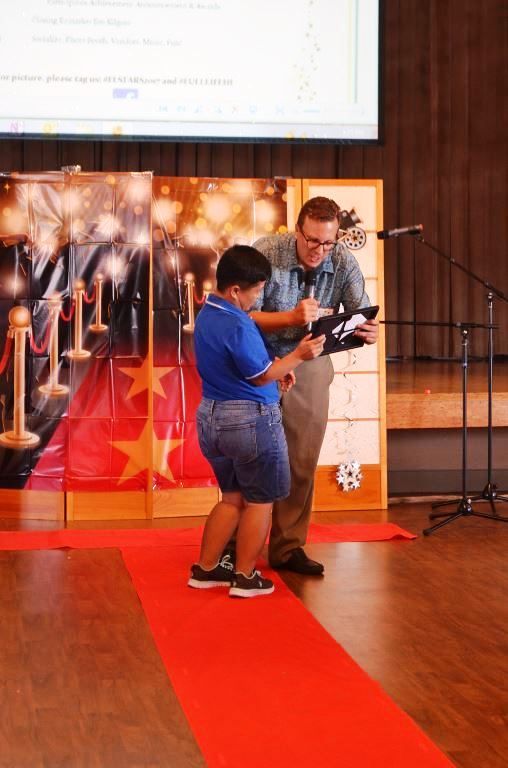 A man and a boy are standing on a red carpet looking at a tablet.