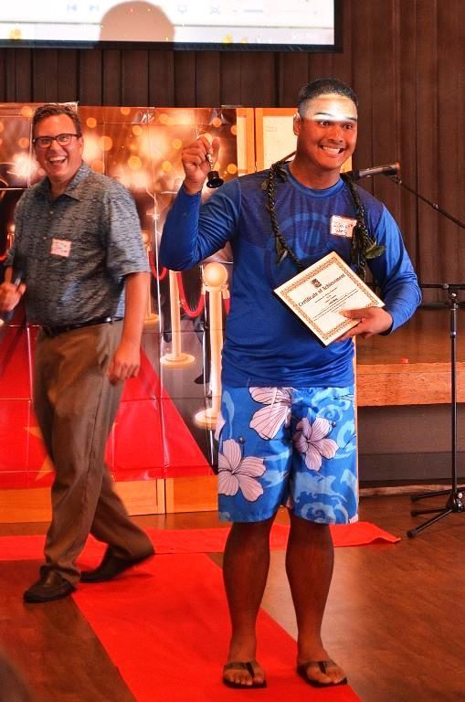A man in a blue shirt and blue shorts is holding a certificate