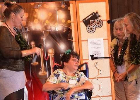 A woman in a wheelchair is talking into a microphone while standing next to other women.