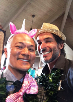 Two men are posing for a picture and one has a unicorn headband on