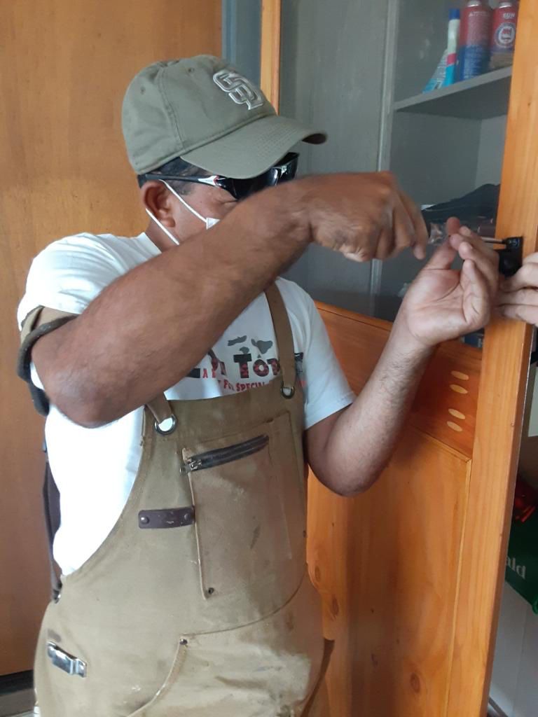 A man wearing overalls and a hat is working on a door.