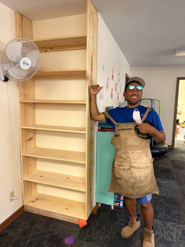 A man is standing next to a wooden shelf in a room.