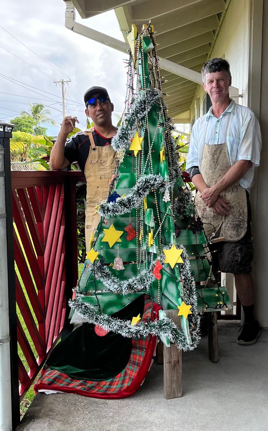 Two men are standing next to a christmas tree made out of plastic bottles.