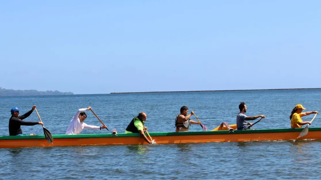 A group of people are paddling a canoe in the ocean.