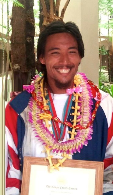 A man with a lei around his neck is holding a framed certificate