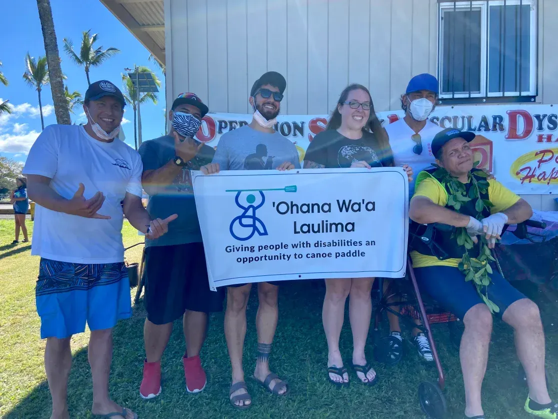 A group of people standing in front of a building holding a sign that says ' ohana wa 'o lauima '