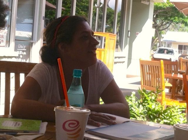 A woman sits at a table with a drink and a bottle of water
