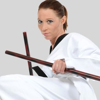 a woman in a white karate uniform is holding two wooden sticks