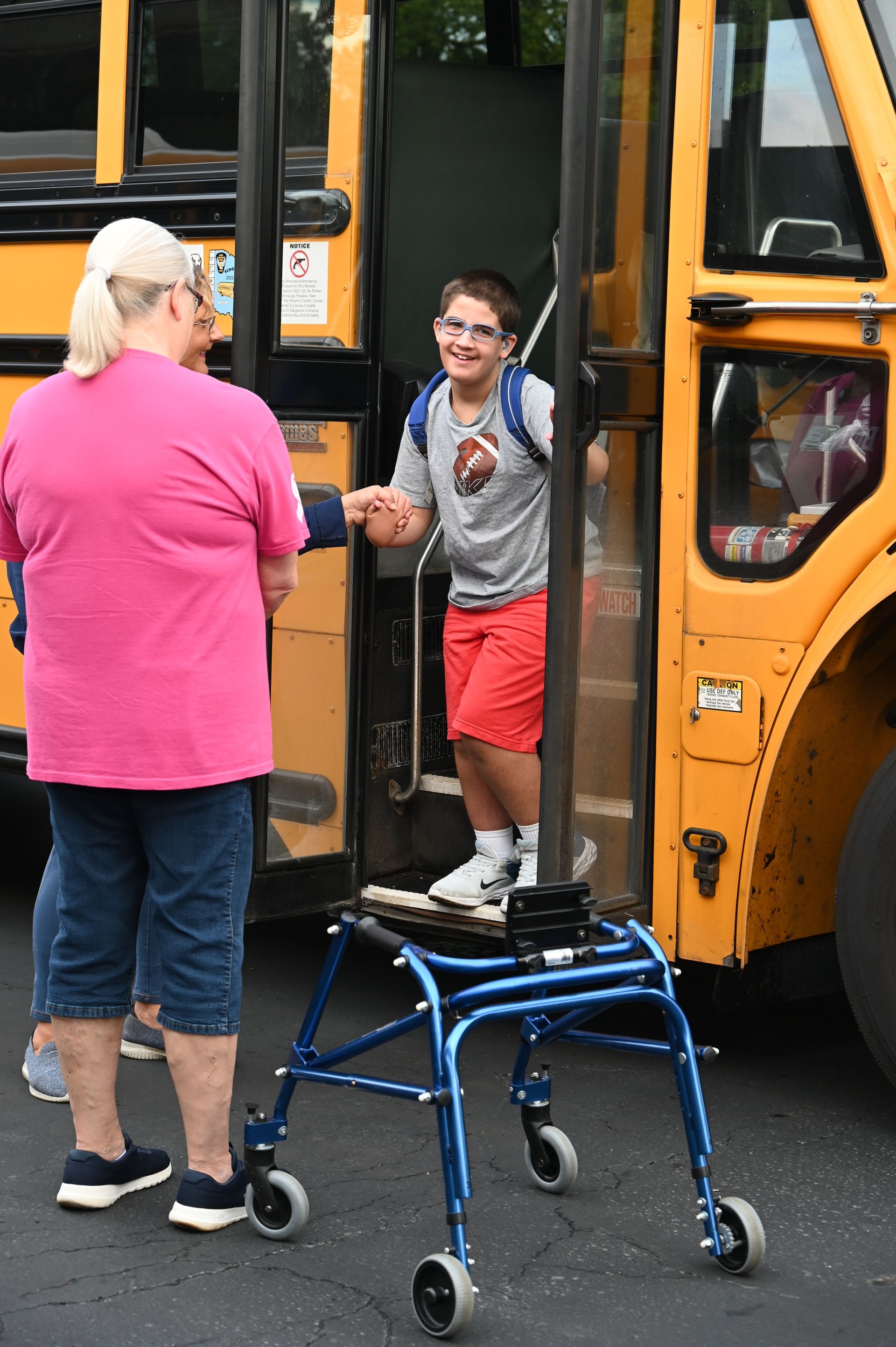 Boy exiting school bus with assistance, using a walker. Woman helps. Smiling.