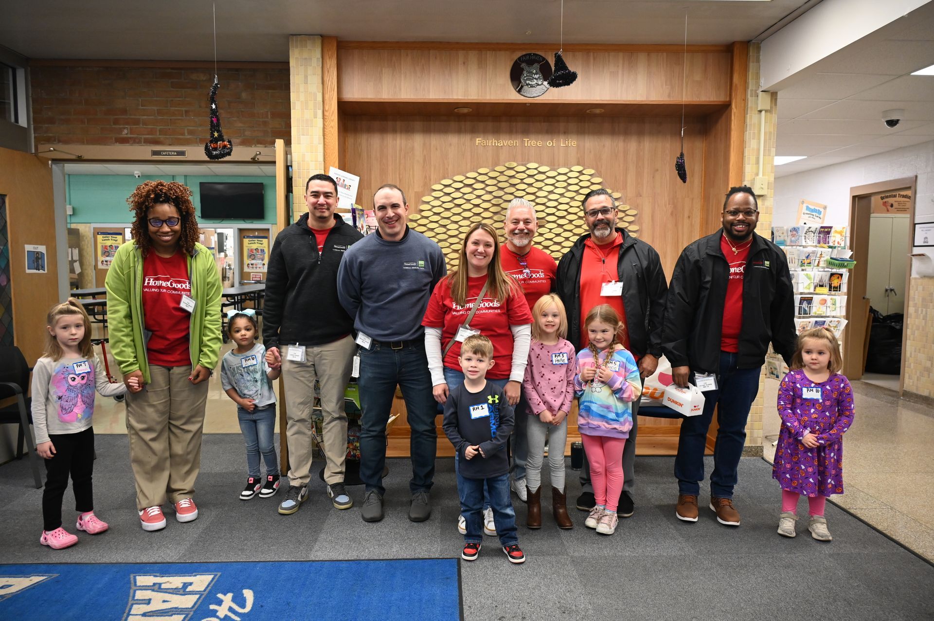 Group of adults and children posing in front of a wooden art piece. Some wear red shirts.