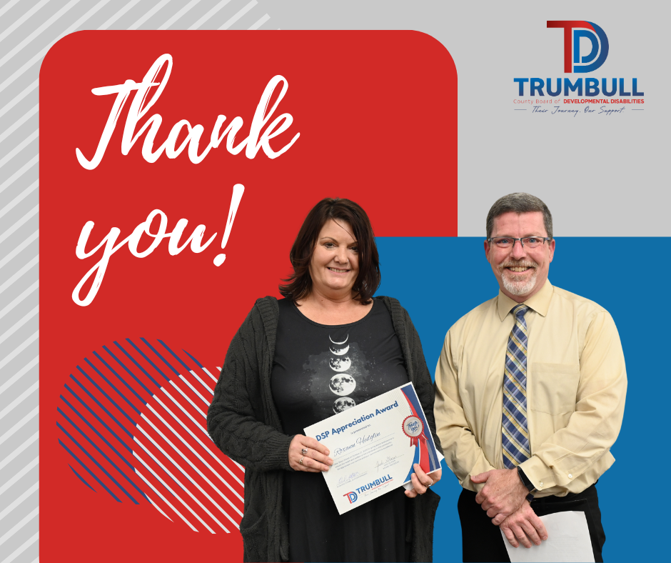 Woman holding award next to man, both smiling in front of a red and blue backdrop with