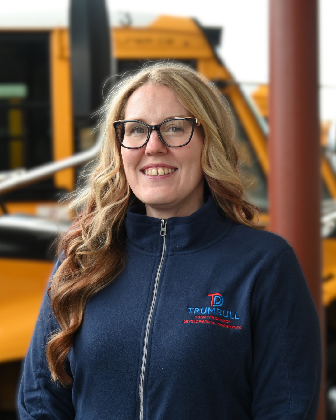 Woman with glasses, blond wavy hair, wearing a black shirt, looking at the camera.