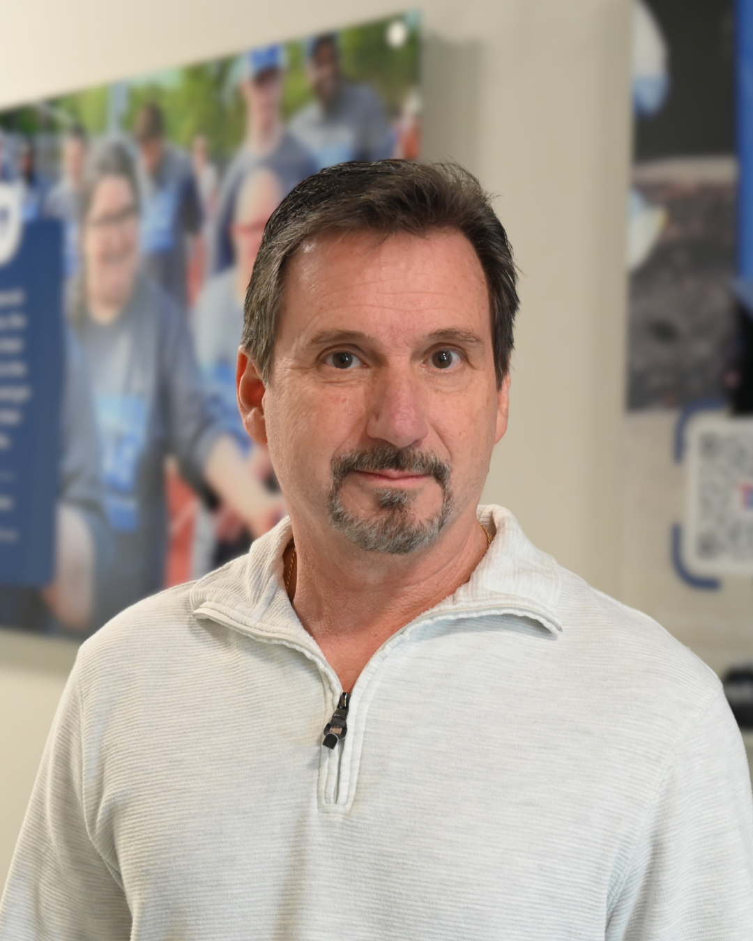 Man with short dark hair, mustache and goatee, wearing a patterned button-down shirt, looking forward.