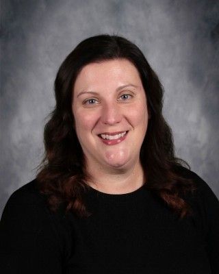 Woman smiling, dark hair, wearing black top, against a mottled gray backdrop.