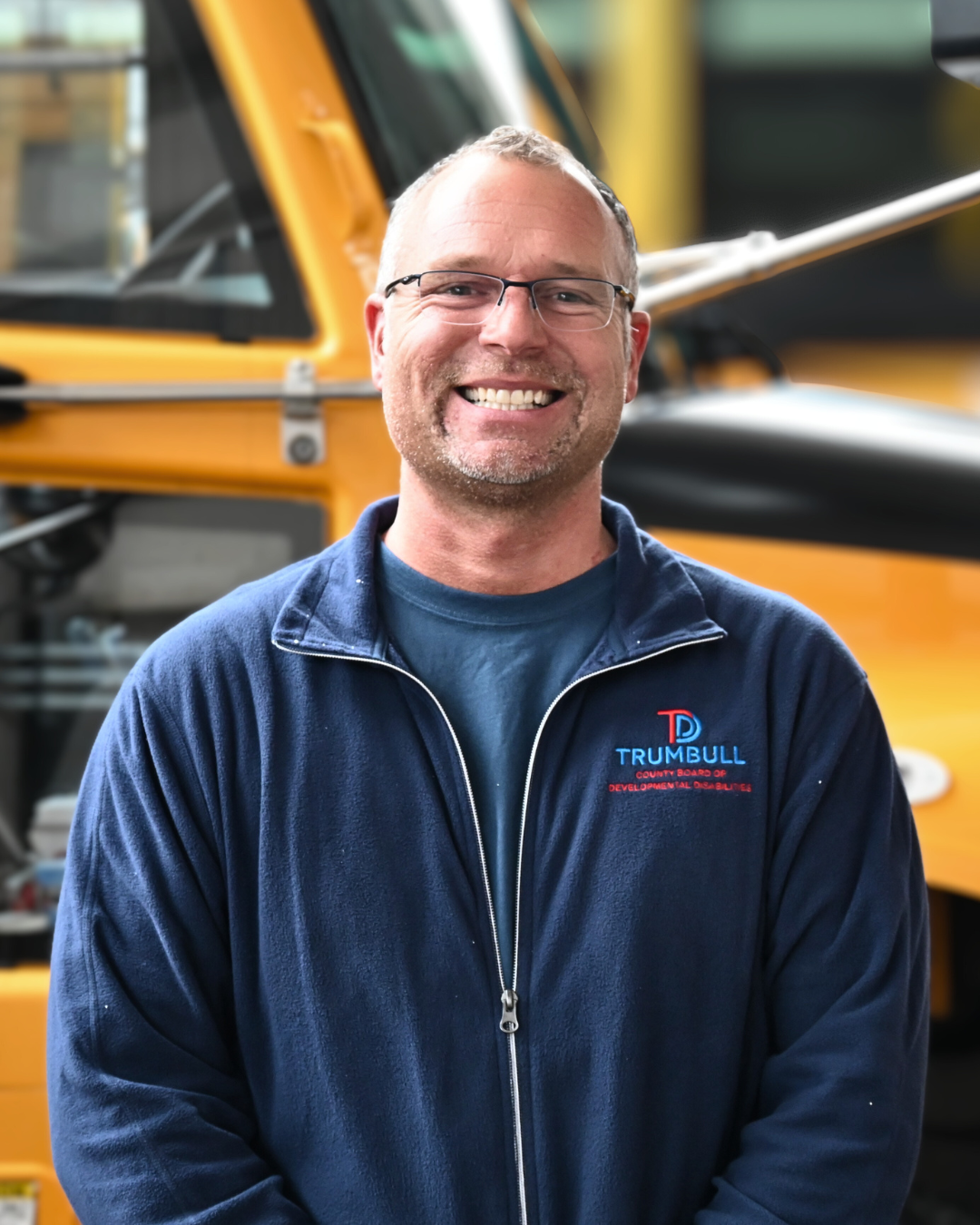 Man in a red sweater smiles, looking at the camera against a blurred background.