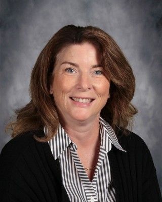 Woman with brown hair smiling, wearing a black sweater over a striped shirt.