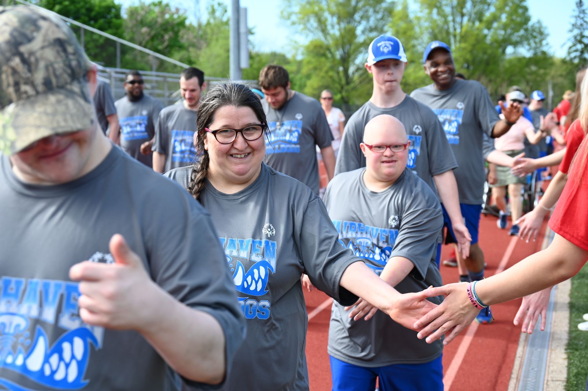 People in gray shirts and blue pants walking on a track, smiling and shaking hands with others.