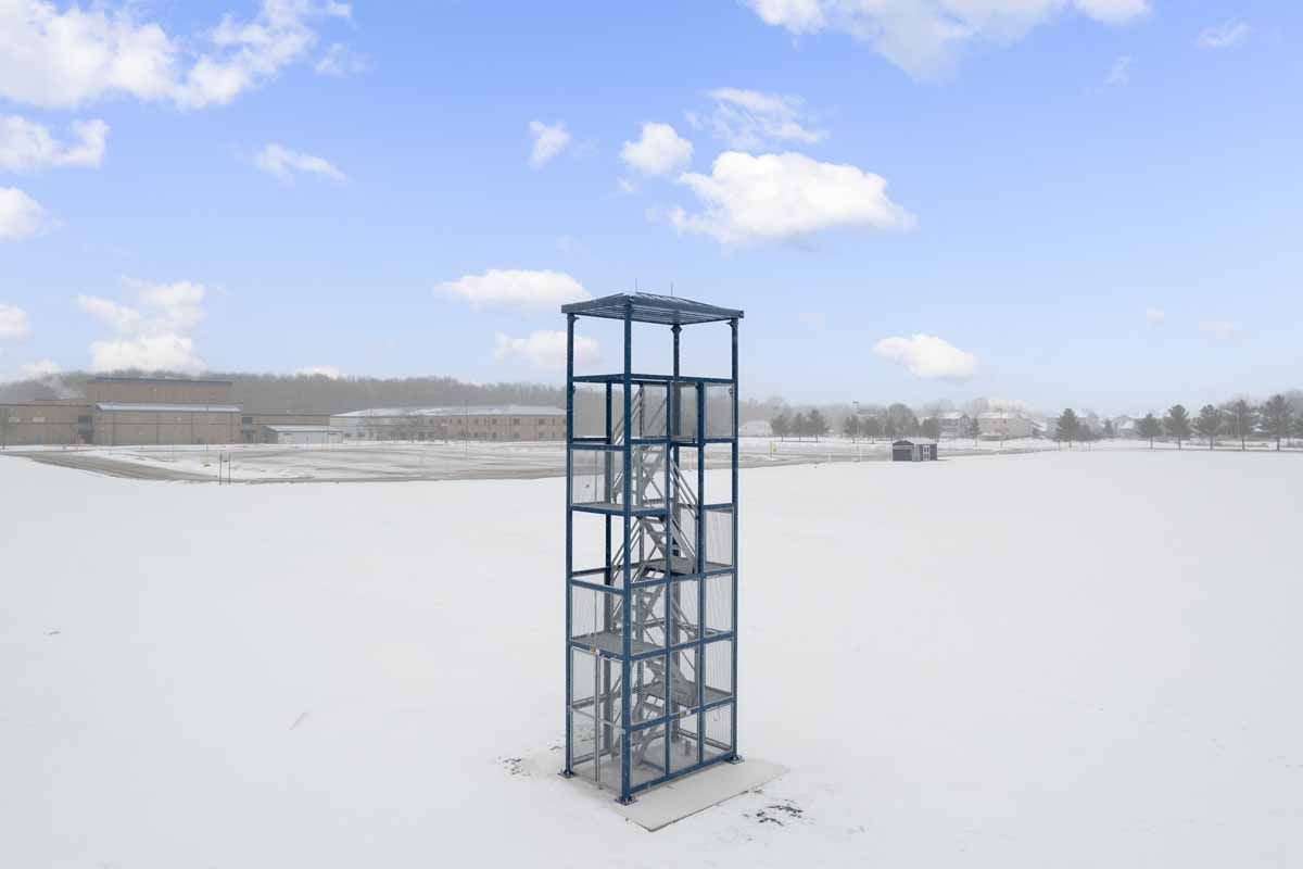Steel observation tower in a snowy field against a backdrop of a hazy blue sky.