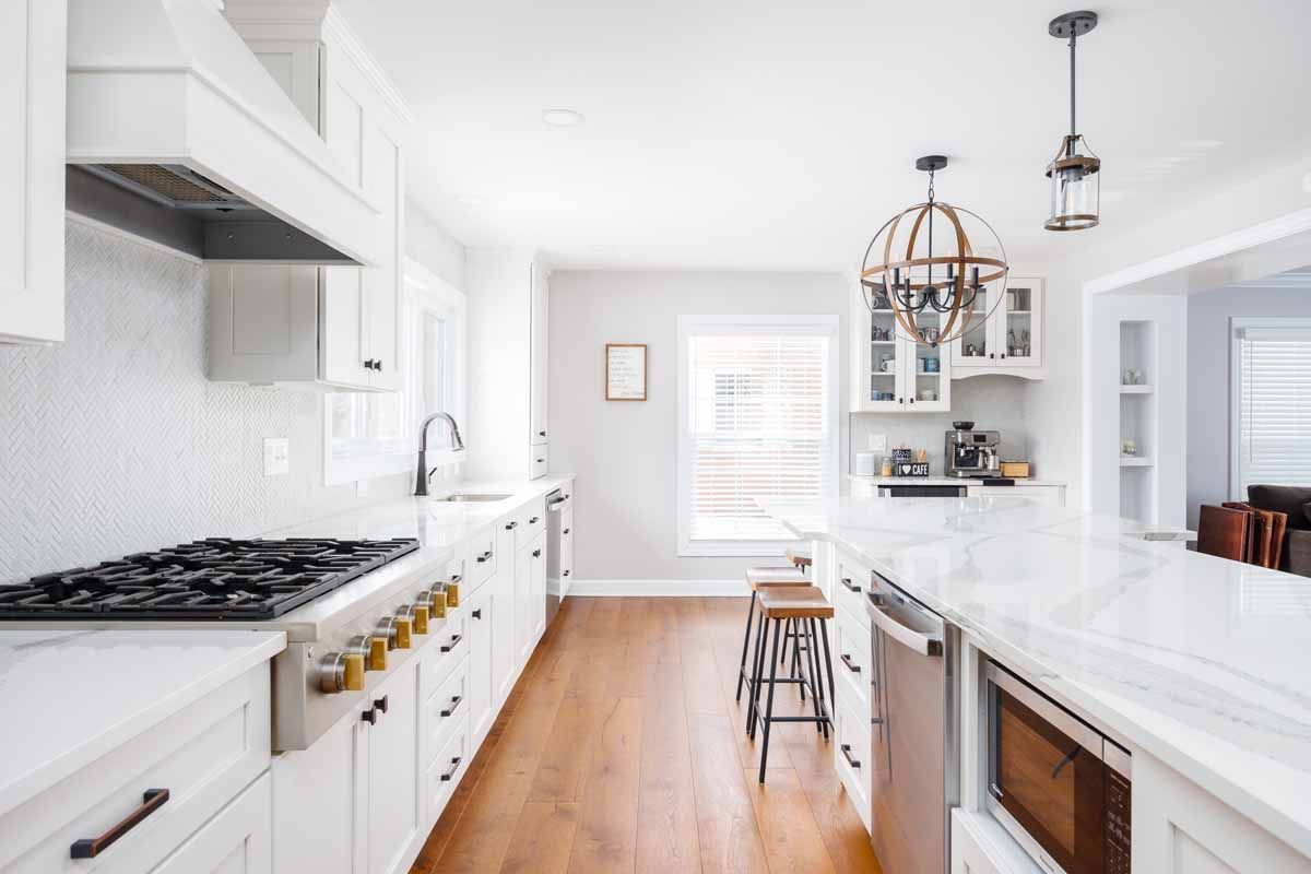 Modern white kitchen with island, wood floors, stainless steel appliances.