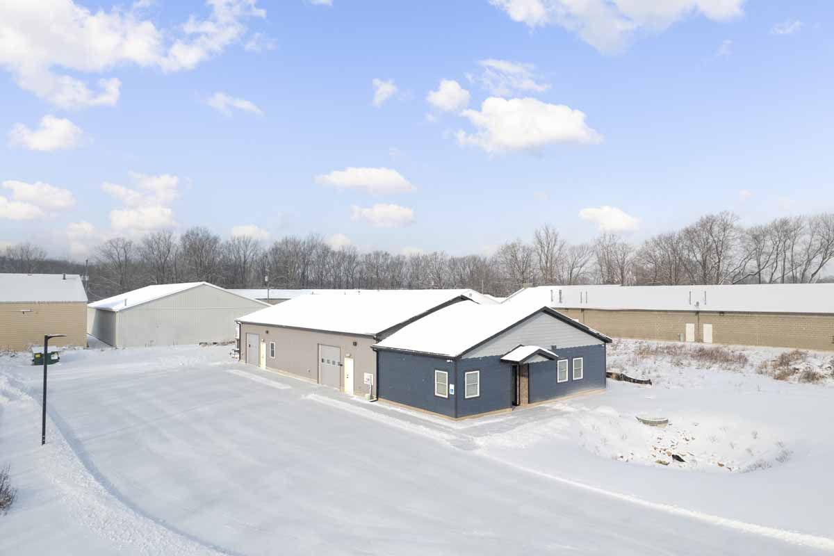 Snow-covered industrial buildings with a dark blue facade under a winter sky.