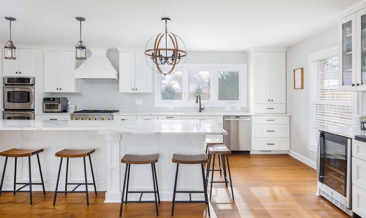 White kitchen with island seating, hardwood floors, and orb light fixture.