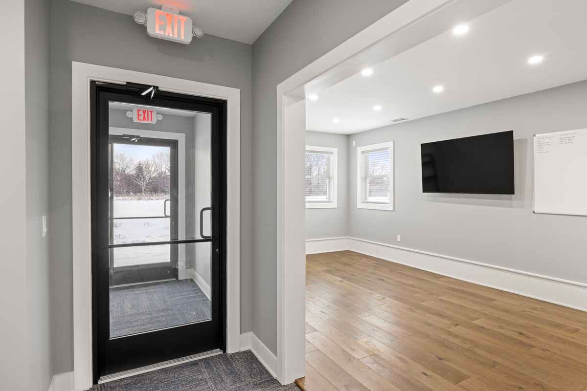 Interior of a building with an entryway, exit door, and a room with a TV and whiteboard.