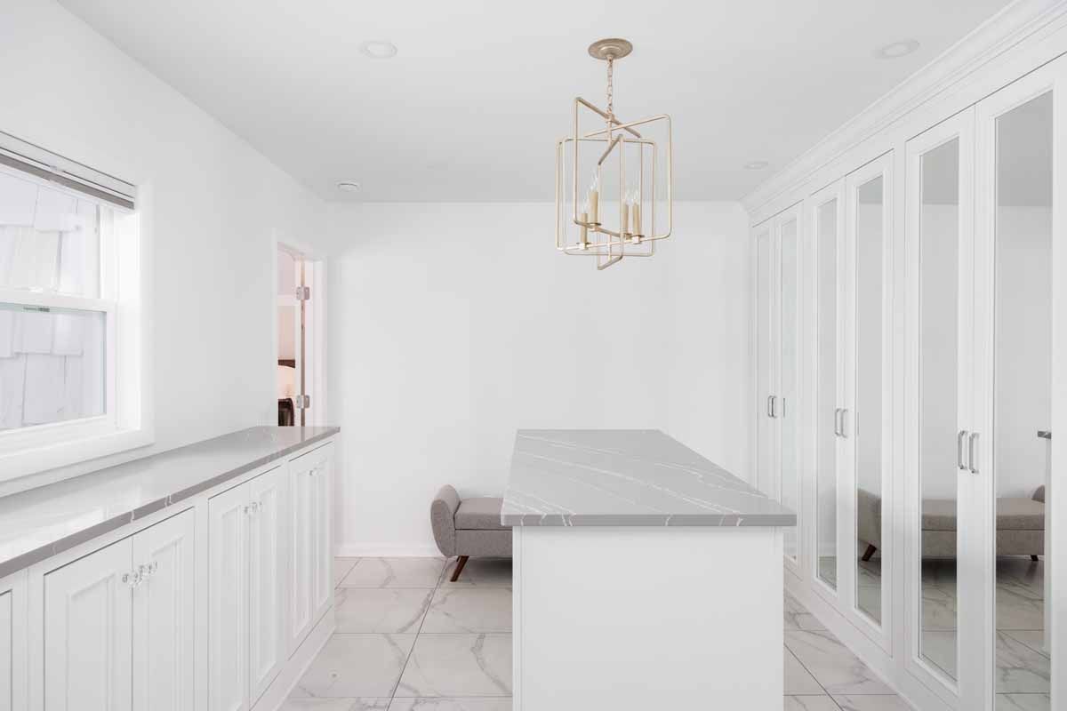 White walk-in closet with a marble countertop island and mirrored doors, a modern chandelier, and a window.