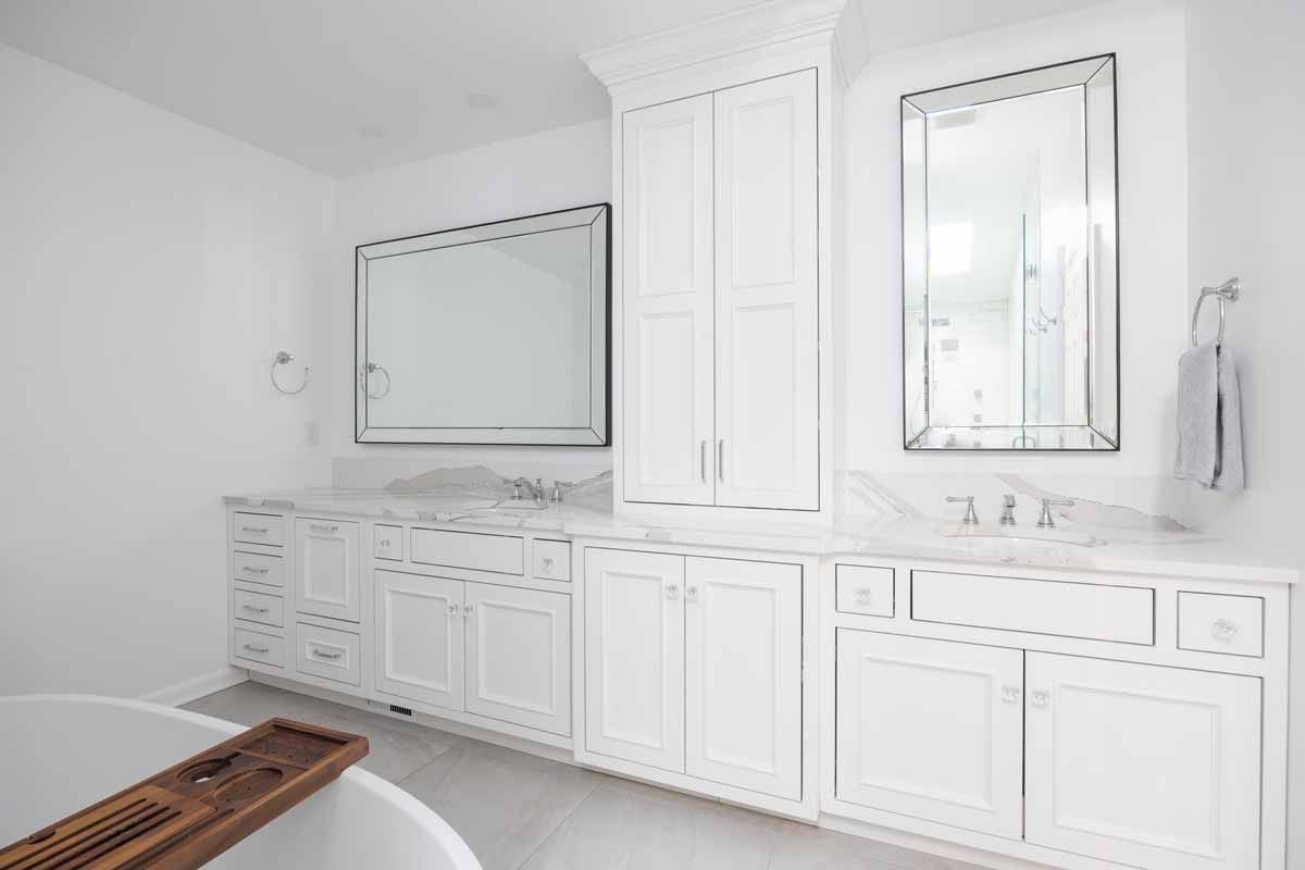 Bright white bathroom with double vanity, central storage, and two mirrors.