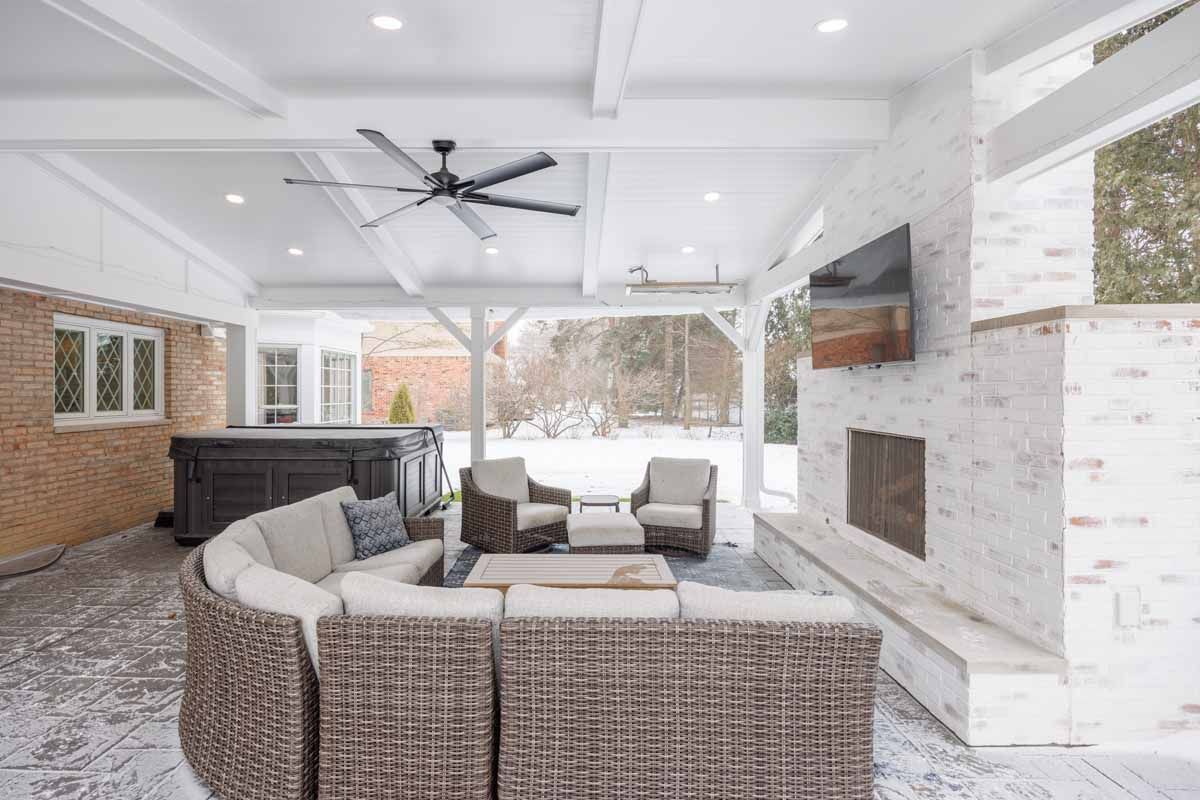 Covered outdoor patio with white-painted brick, fireplace, seating, and hot tub; snow visible.