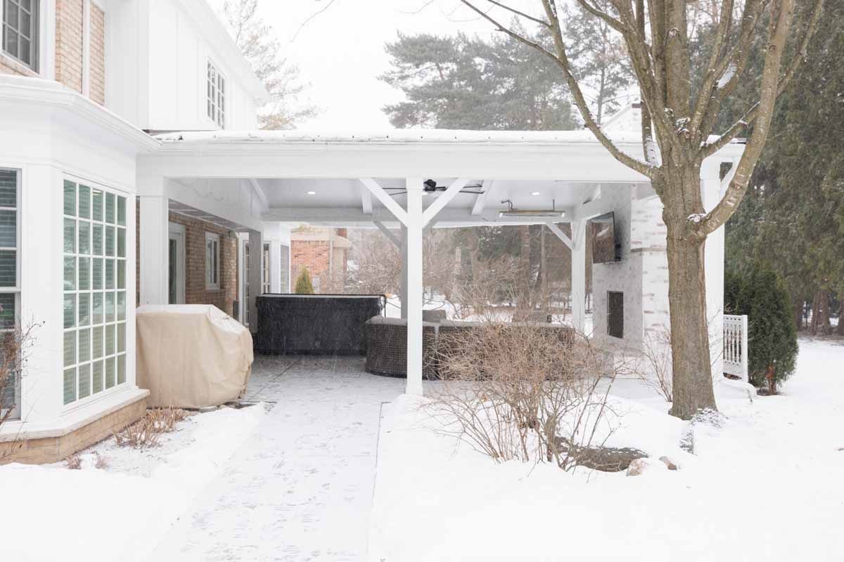 Snowy outdoor patio with a white pergola and covered bar area.