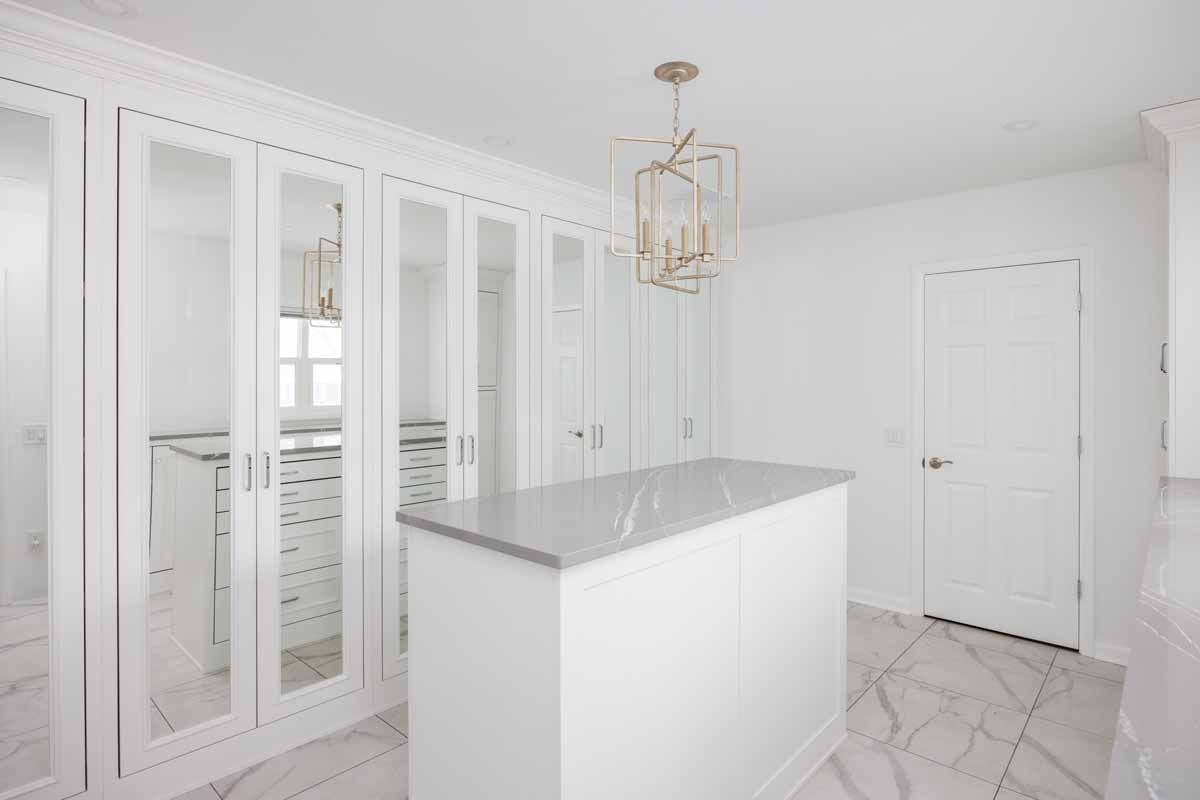 White walk-in closet with mirror-panelled doors, an island with a marble countertop, and a chandelier.