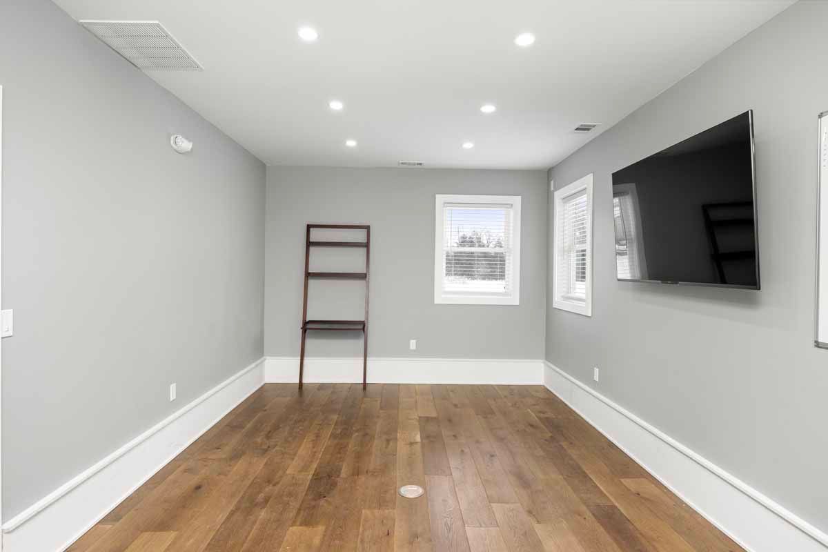 Empty room with wood floor, gray walls, window, and a mounted TV. A wooden ladder leans against one wall.
