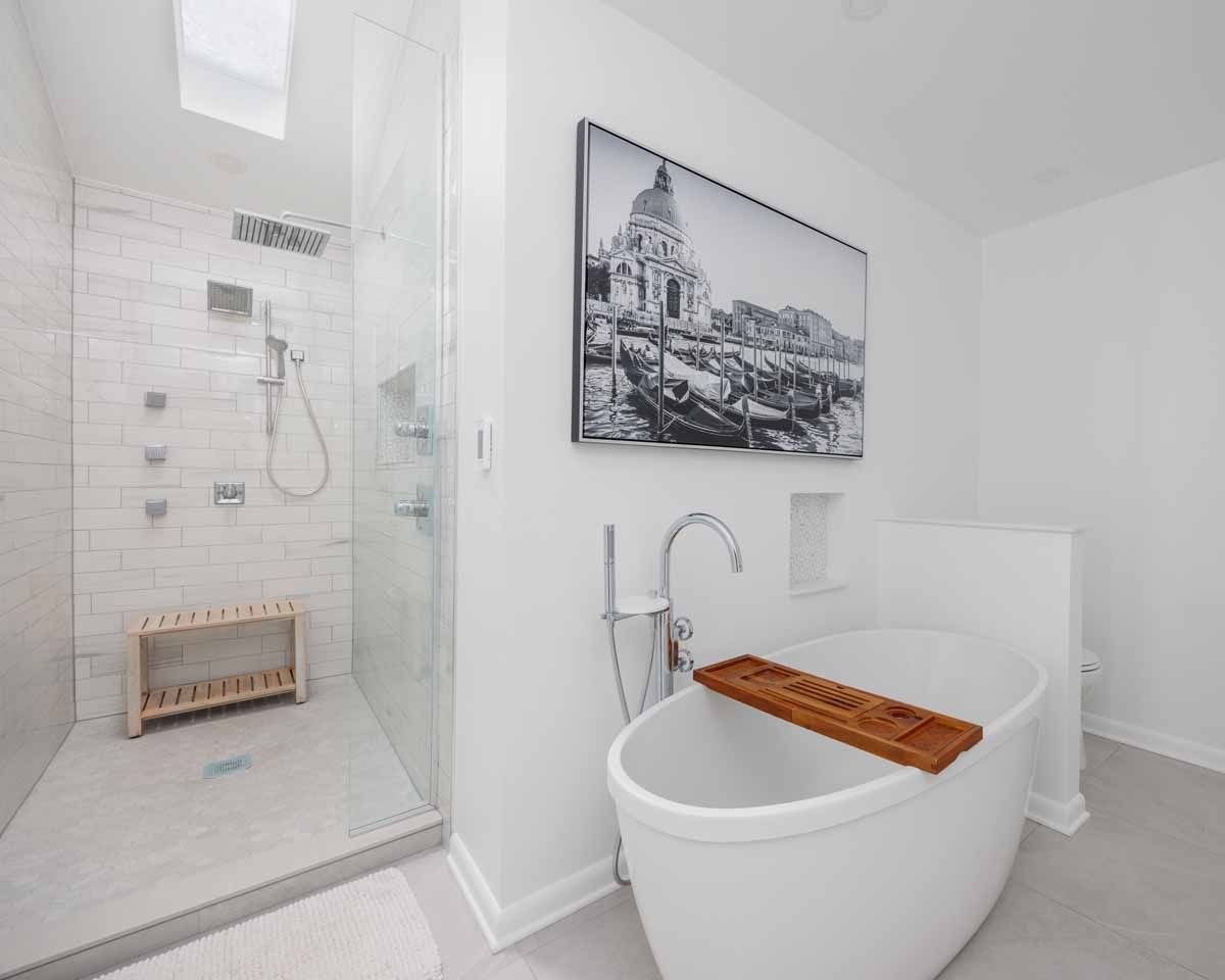 White bathroom with glass shower, freestanding tub, and black and white artwork.