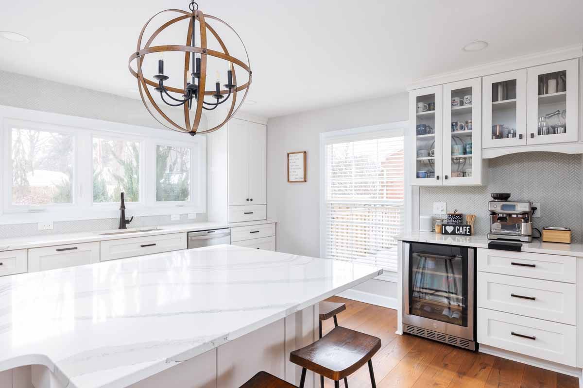 Bright white kitchen with large island, wooden floors, and globe chandelier.