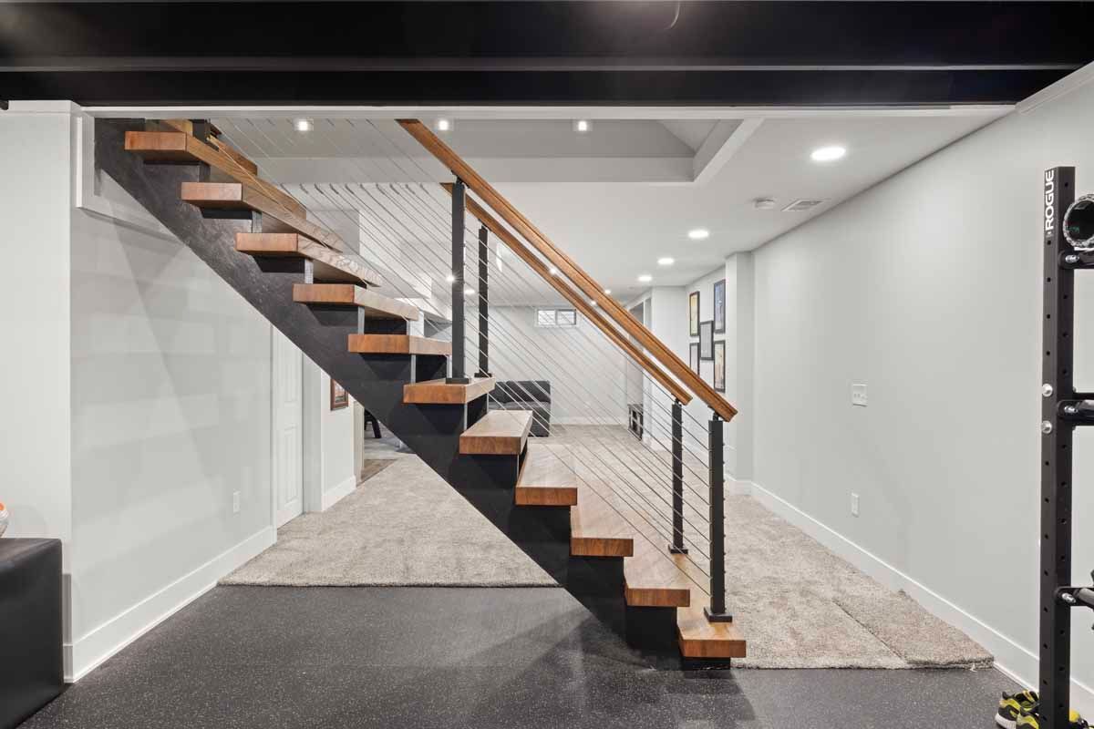 Modern staircase with wooden steps, black metal frame, and white cable railing leads to a basement.