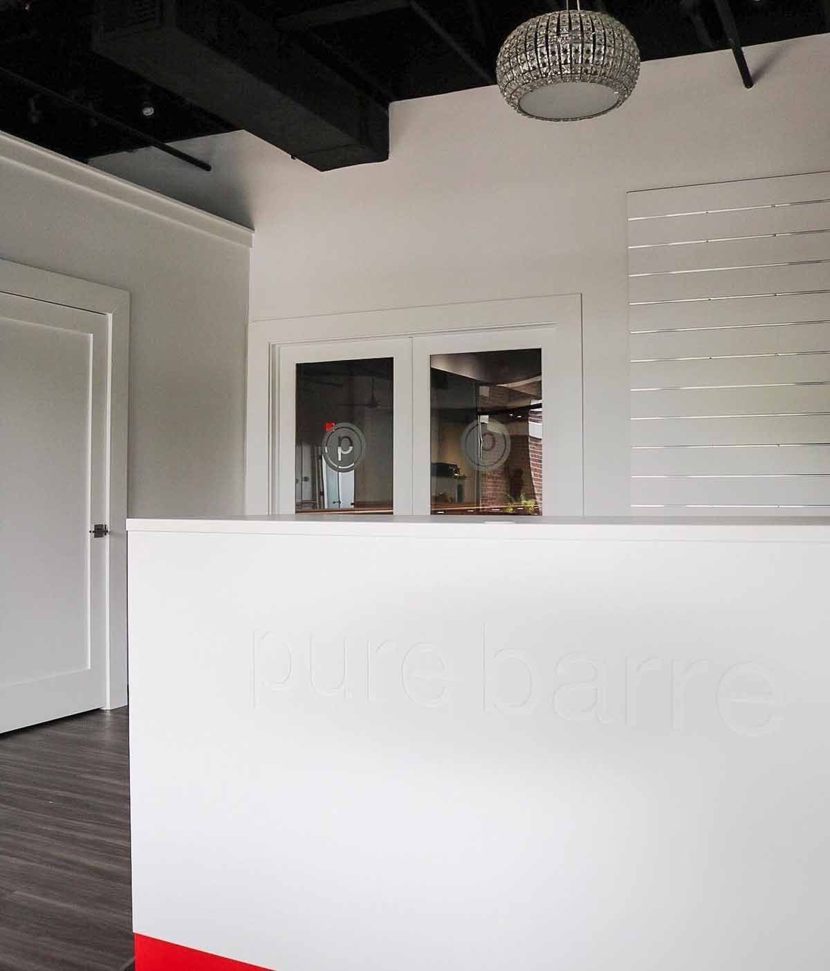 White reception desk in a bright office space with a glass door and overhead chandelier.