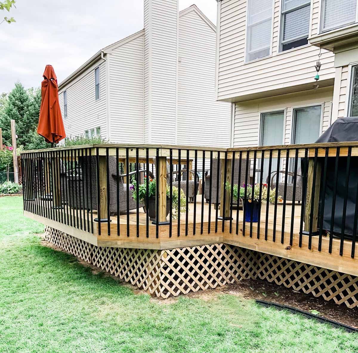 Wooden deck with black railing, lattice skirting, and orange umbrella in a backyard.
