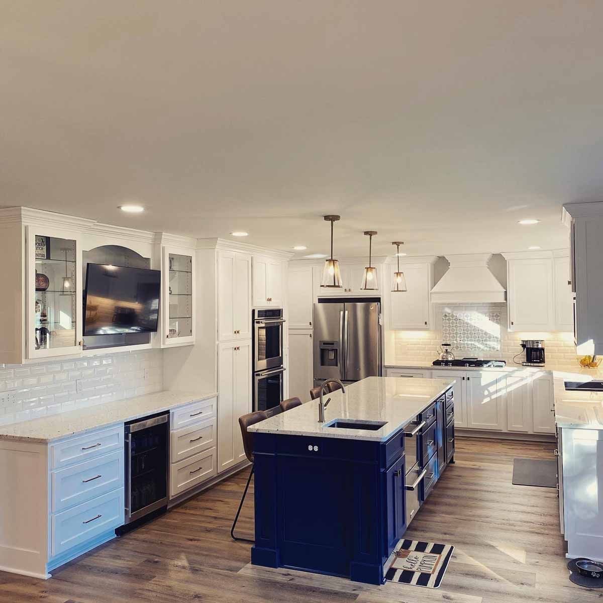 Spacious modern kitchen with blue island, white cabinets, stainless steel appliances, and wood flooring.
