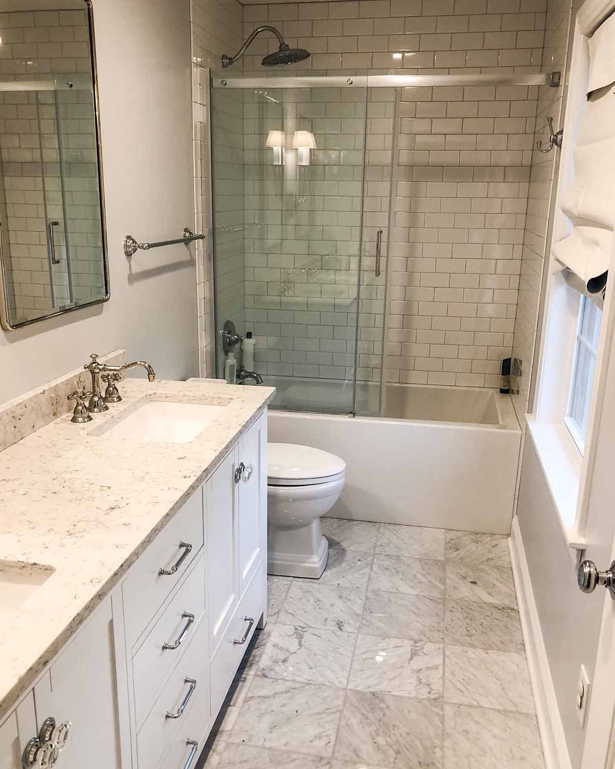 Bathroom with white subway tile, marble floors, white vanity, glass shower door.