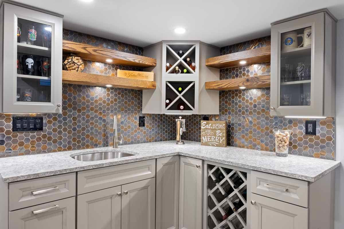 Corner bar area with grey cabinets, wooden shelves, mosaic tile backsplash, and granite countertop.