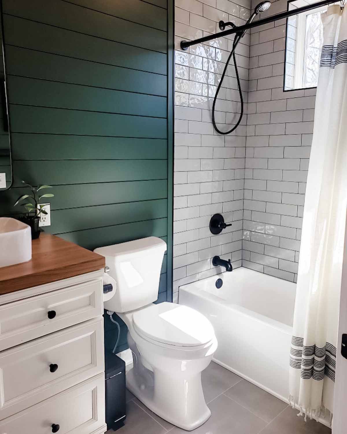 Bathroom with a dark green shiplap wall, white subway tile, white toilet, and black fixtures.