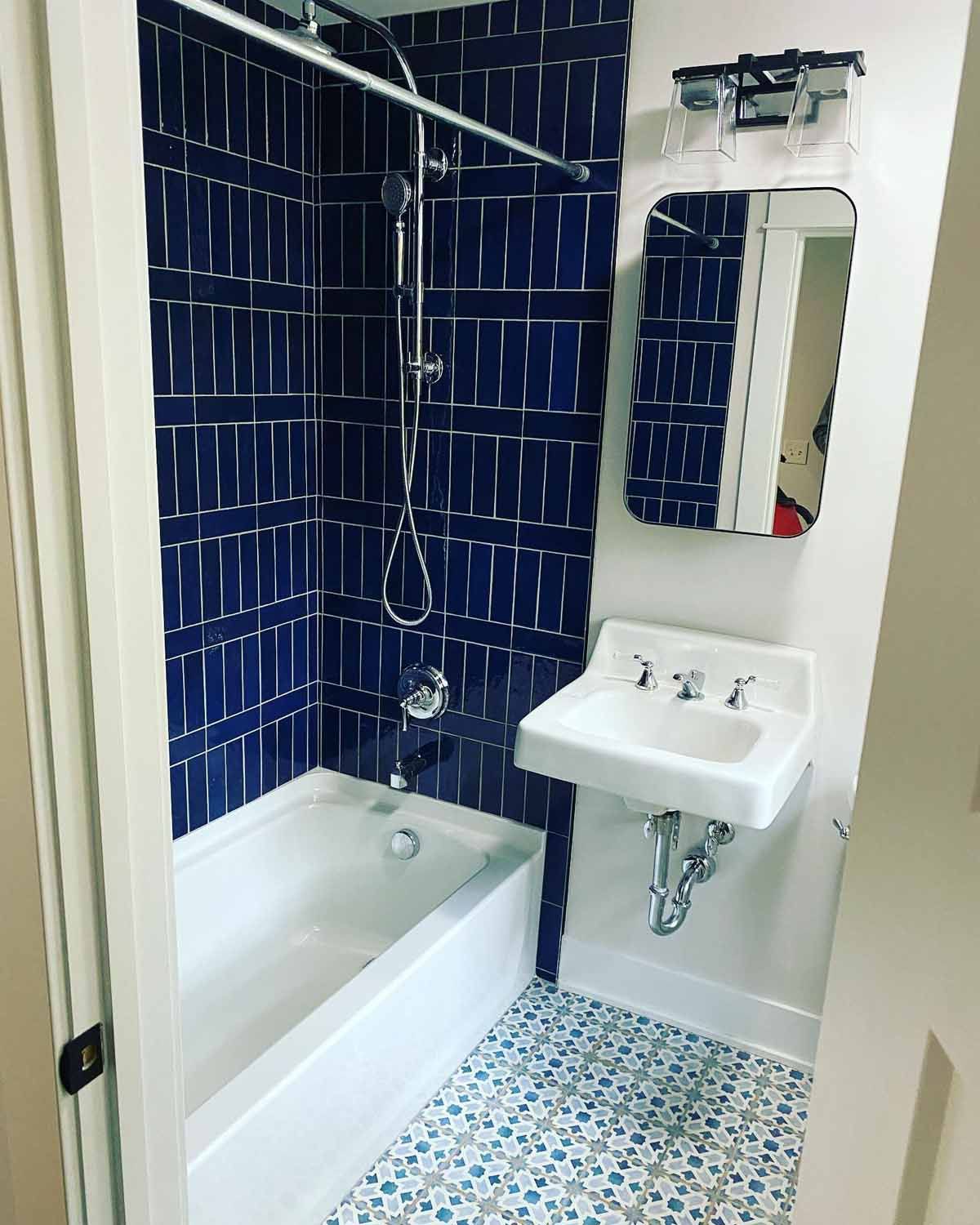 Small bathroom with blue tile shower and patterned floor. White sink and tub.